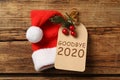 Tag with text Goodbye 2020 and Santa hat on wooden background, flat lay Royalty Free Stock Photo