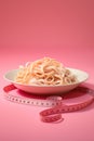 Tagliatelle pasta with measuring tape on pink background. Diet concept. Royalty Free Stock Photo