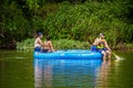 Tahlequah OK USA Blue inflatable raft on river with couple sitting at back and man in tie dye tee shirt sitting on side