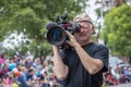 older professional photographer with cap turned backward and stubbly whiskers squints into viewfinder of