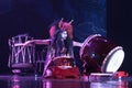 Taiko drummer in a wig and a demon mask performs on stage with drum on a dark background