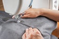 Tailor hands stitching gray fabric on modern sewing machine at workplace in atelier