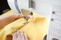 Tailor hands stitching yellow fabric on modern sewing machine at workplace in atelier