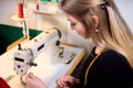 Tailor laboring at working place in atelier. Sewing machine, ruler, scissors, table lamp, threads on background.