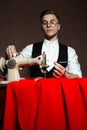 Tailor in round glasses sits at a table with a sewing machine