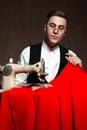 Tailor in round glasses sits at a table with a sewing machine