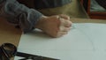 The tailor`s hand with a pencil draws the shape of the patterns for the author`s shoes on paper.