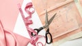 Tailoring concept. Accessories for sewing and needlework. Scissor, measuring tape, thread and pink satin fabric and pattern on