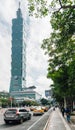 Taipei 101 building with tree branches on the right side and cars on the road from below with bright blue sky and cloud in Taipei