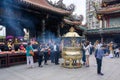 Taipei, Longshan Temple, Taiwan. People praying and offering incense sticks in golden burner.