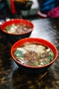 Taiwanese style handmade noodle with steamed beef stew and wontons in hot soup in red, black bowl, famous street food in Jiufen.