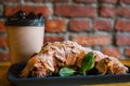 Take away coffee and fresh croissant with mint on wooden background. Cardboard cup with face cap concept Royalty Free Stock Photo