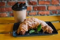 Take away coffee and fresh croissant with mint on wooden background. Cardboard cup with face cap concept Royalty Free Stock Photo