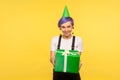 Take birthday present! Portrait of generous cute hipster girl wearing funny party cone giving present box, congratulating. studio