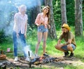 Take a break to have snack. Company hikers at picnic roasting sausages on sticks. Friends prepare roasted sausages