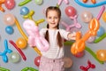 Take it. Having fun on party. Smiling cute little girl with braids standing against gray decorated wall, giving her multicolored Royalty Free Stock Photo