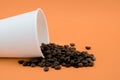 Take-out coffee cup with spilled coffee beans, orange background