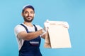 Take it! Portrait of friendly smiling handyman in overalls and gloves giving ordered parcel