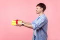 Take it! Portrait of positive generous brown-haired man giving present to the left. isolated on pink background