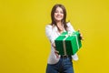 Take this present. Portrait of generous brunette woman holding out gift and smiling at camera. isolated on yellow background