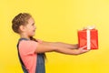 Take it! Side view of cute little girl looking up and giving decorated present, generous child sharing christmas gift