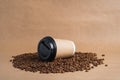 Takeaway brown paper coffee cup with black cap lie on roasted beans at brown background. Mock up Royalty Free Stock Photo