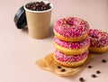 Takeaway coffee cup with coffee beans and pink glaze donuts with colorful sprinkles, pink background Royalty Free Stock Photo