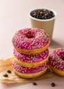 Takeaway coffee cup with coffee beans and pink glaze donuts with colorful sprinkles, pink background Royalty Free Stock Photo