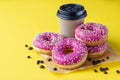 Takeaway coffee cup with coffee beans and pink glaze donuts with colorful sprinkles, pink background Royalty Free Stock Photo