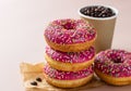 Takeaway coffee cup with coffee beans and pink glaze donuts with colorful sprinkles, pink background Royalty Free Stock Photo