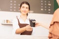 Takeaway coffee cup in two hands of customer and beautiful caucasian barista woman who looks at other customers, focusing at