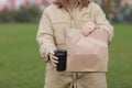 Takeaway cup with coffee, mock up for identity branding. Close-up of paper bag and paper cup in female hand.Young woman carries