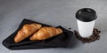 Takeaway food. Two fresh croissants lie on a dark napkin. Nearby is a white paper cup with coffee Royalty Free Stock Photo