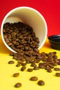 Takeaway paper coffee cup with black cap on red and yellow background with pouring roasted beans Royalty Free Stock Photo