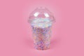 Takeaway plastic cup with dome for cold drinks filled with colorful sugar balls on pink background. Rainbow colored candies, sweet Royalty Free Stock Photo