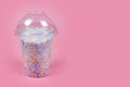 Takeaway plastic cup with dome for cold drinks filled with colorful sugar balls on pink background. Rainbow colored candies, sweet Royalty Free Stock Photo
