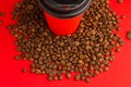 Takeaway red paper coffee cup with black cap stand on roasted beans at red background. Mock up Royalty Free Stock Photo