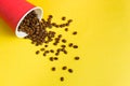Takeaway red paper coffee cup on yellow background with pouring roasted beans out of it Royalty Free Stock Photo