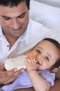 He takes his role as a father seriously. A father feeding his baby boy a bottle of milk while sitting on the sofa. Royalty Free Stock Photo