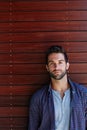 Taking it all in his stride. Portrait of a handsome man standing against a wooden wall. Royalty Free Stock Photo