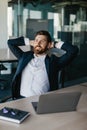 Taking break from work. Excited businessman relaxing on chair, leaning back at workplace and holding hands behind head Royalty Free Stock Photo
