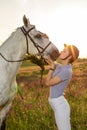 Jockey young girl petting and hugging white horse in evening sunset