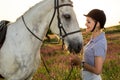 Jockey young girl petting and hugging white horse in evening sunset