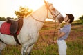 Jockey young girl petting and hugging white horse in evening sunset