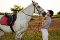 Jockey young girl petting and hugging white horse in evening sunset