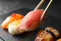 Taking delicious nigiri sushi with chopsticks from serving board on black table, closeup Royalty Free Stock Photo