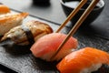 Taking delicious nigiri sushi with chopsticks from serving board on black table, closeup Royalty Free Stock Photo