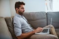 Taking it easy today. a focused young man working on his laptop while being seated on a couch at home during the day.