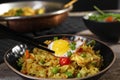 Taking egg with chopsticks from bowl with tasty rice, meat and vegetables on wooden table, closeup