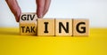 Taking or giving symbol. Hand turns a cube and changes the word `taking` to `giving` on wooden cubes. Beautiful yellow table, Royalty Free Stock Photo